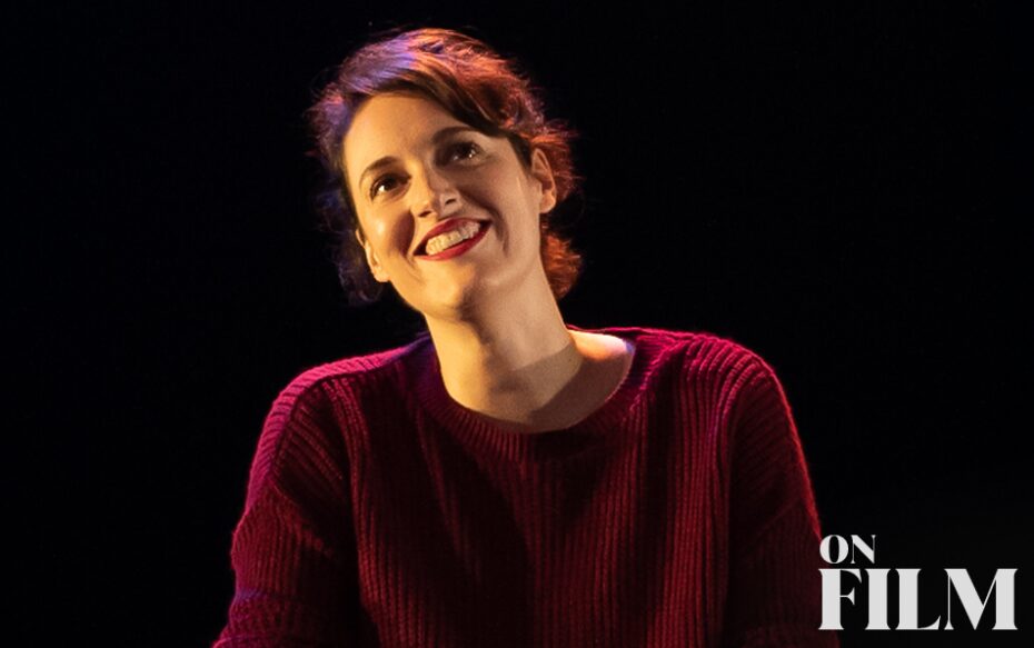 Phoebe smiles happily onstage in a maroon sweater in front of a black background