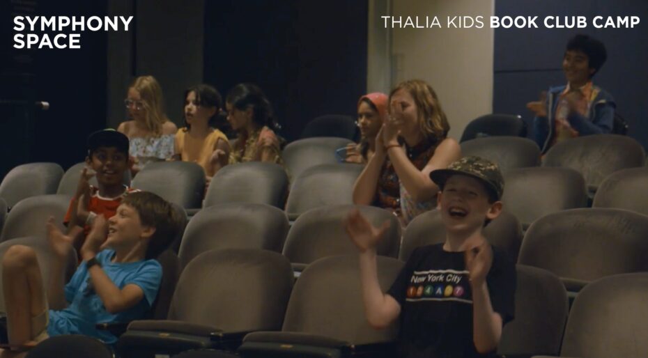 Campers are sitting in a theater while smiling and clapping their hands - this links to a video.