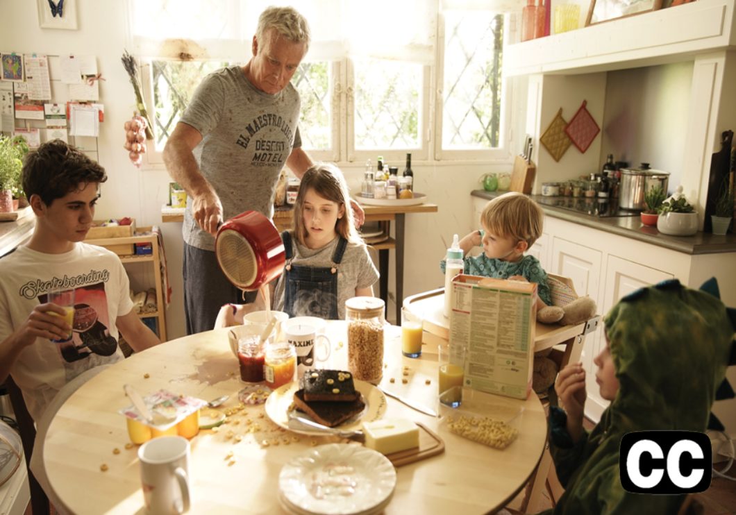 Kitchen scene with dad holding a red pot with four children around the table of various ages.