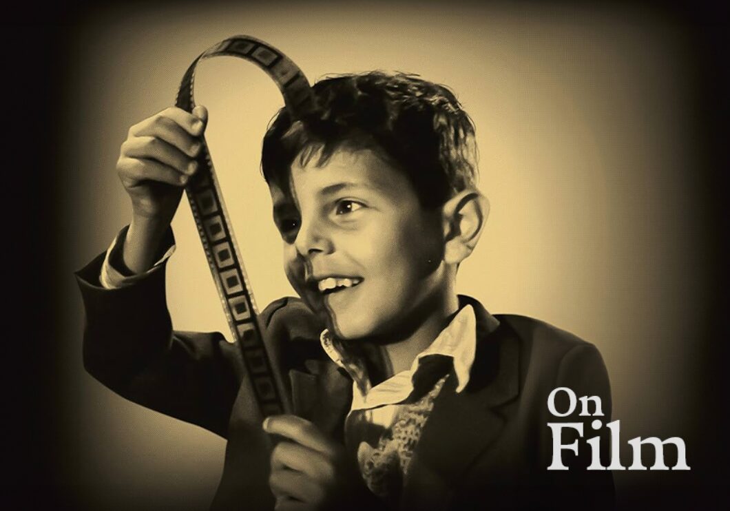 A black and white image of a boy looking at a piece of film.