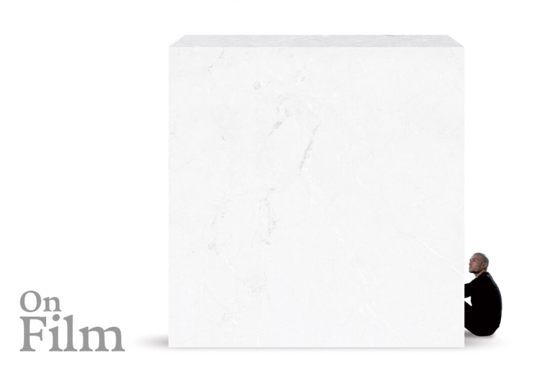 A white marble block with a man sitting next to it.