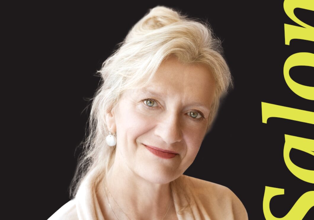 In front of a black background, Elizabeth Strout stands next to the word 'Salon.'