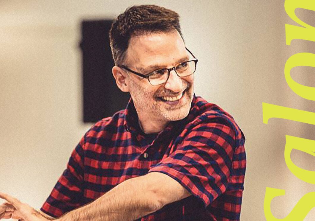Joel Fram smiles as he conducts, with 'Salon' written in yellow lettering.