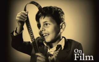A black and white image of a boy looking at a piece of film.