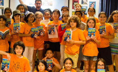 A group of Thalia Book Club camp kids in orange t-shirts hold up books.